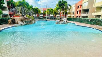 A swimming pool with clear water, surrounded by palm trees and a building with balconies.