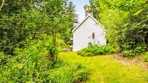 A white building with a sloped roof and a chimney, surrounded by dense green foliage. - Vacation home Dancot by Interhome (Drumnadrochit)