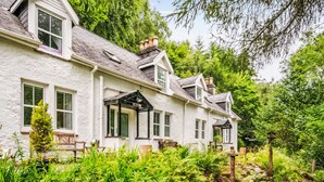 A white house with multiple windows and a porch, surrounded by lush greenery. - Vacation home Dancot by Interhome (Drumnadrochit)