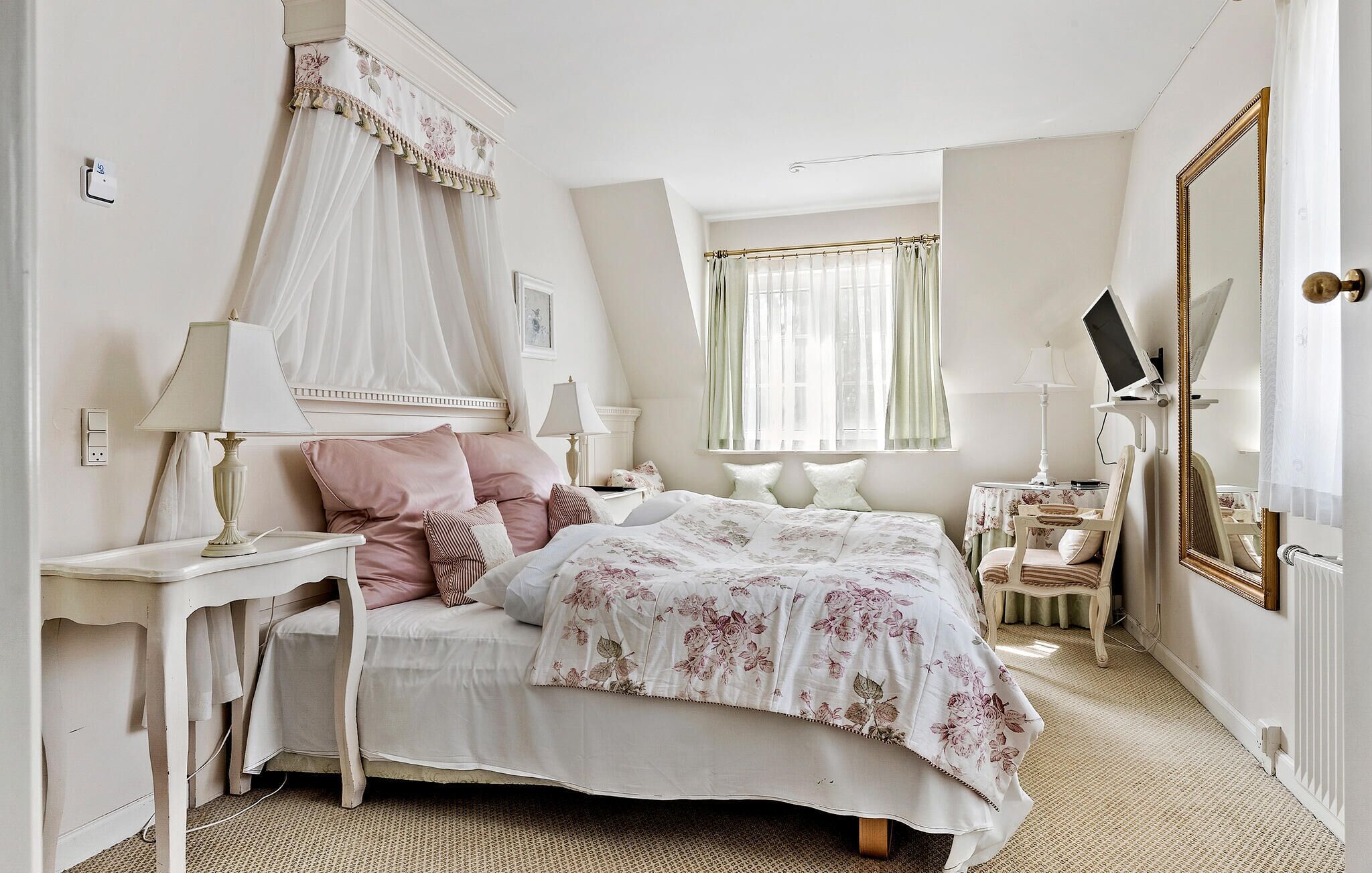 A bedroom with a canopy bed, bedside tables, a chair, a mirror, and a television.