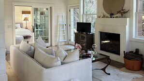 Un salon spacieux avec un canapé blanc, un pouf moelleux, une cheminée et un grand miroir.