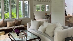 Un salon spacieux avec un plafond haut, des murs en bois peints en blanc, un grand canapé, une table basse en verre et un tapis en cuir.