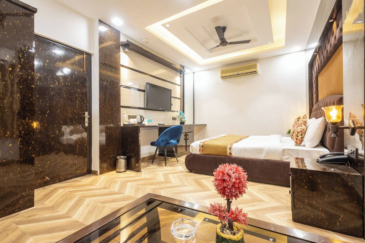 A modern hotel room with a wooden herringbone floor, a bed with a brown headboard, a desk with a chair, a television, and a ceiling fan.