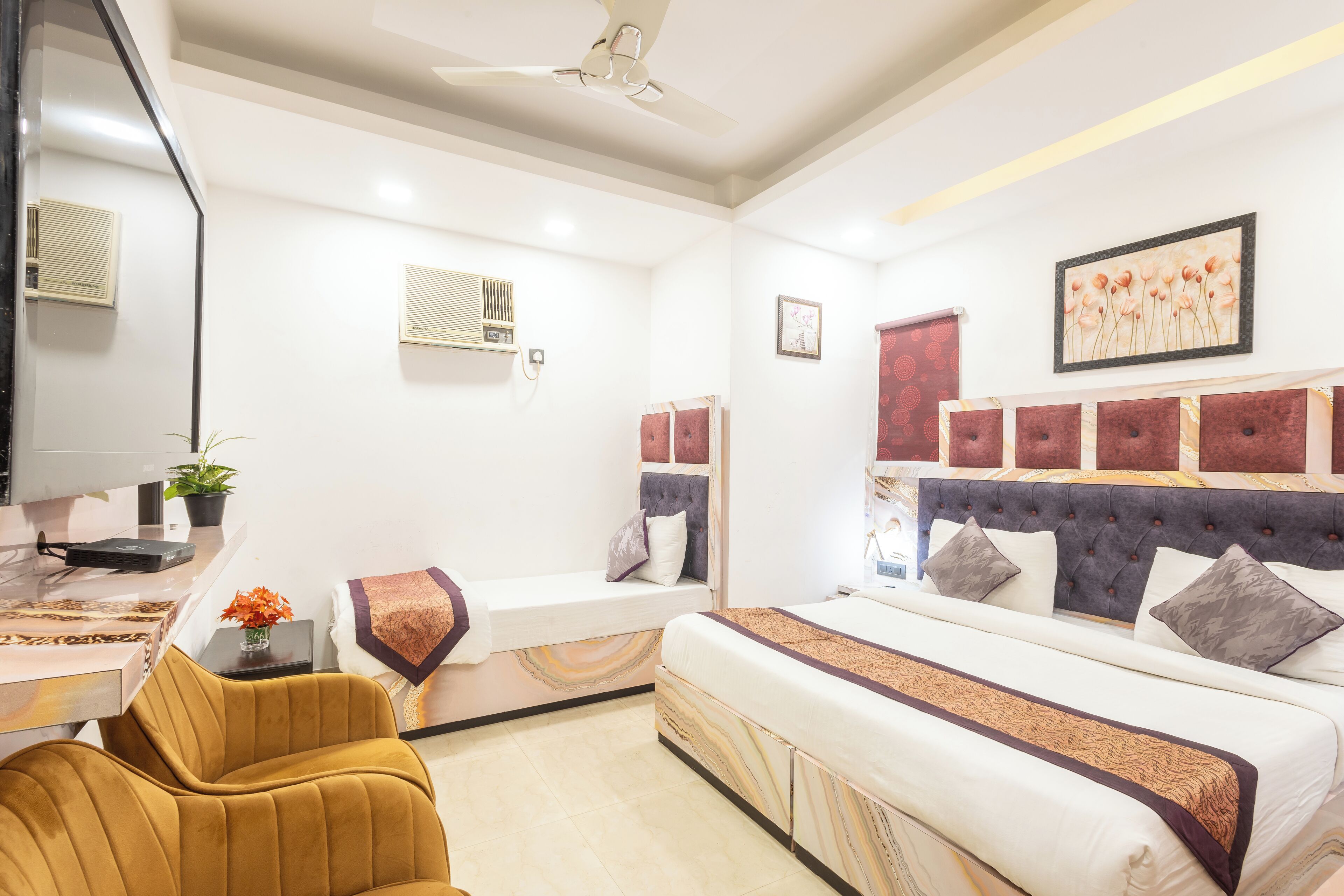 A modern hotel room with a large bed, a sofa, a small table with a plant, and a TV.
