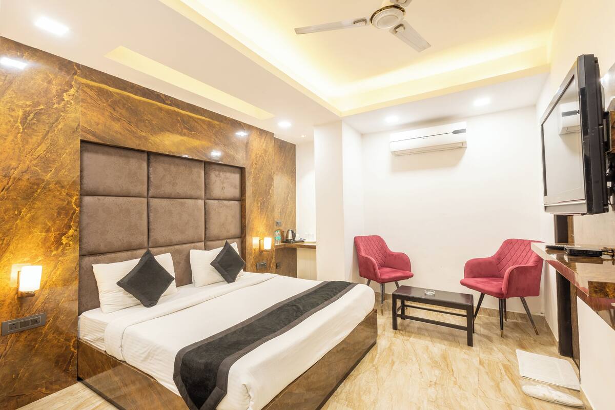 A modern hotel room with a large bed, a desk, two chairs, a ceiling fan, and an air conditioning unit.