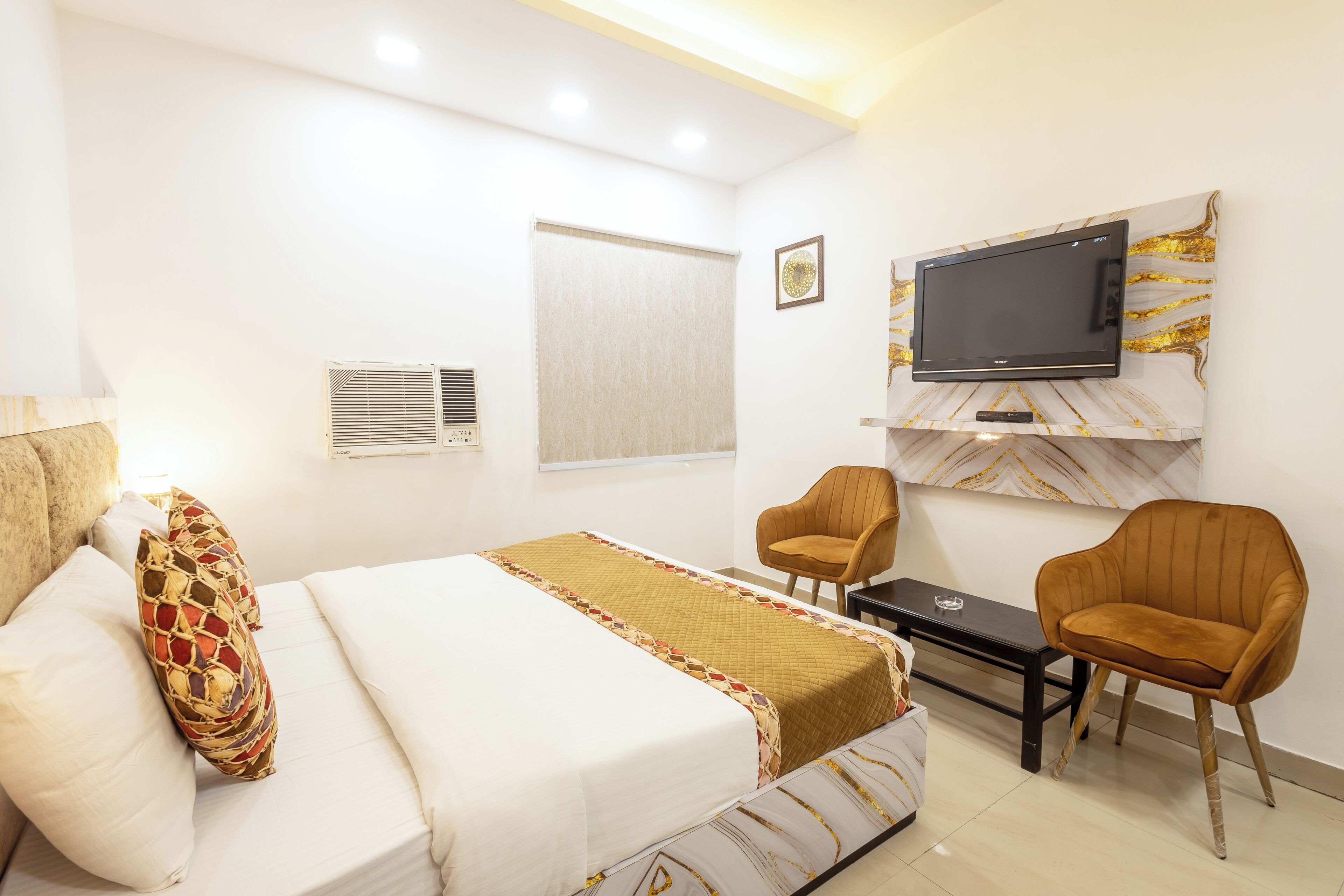 A hotel room with a bed, two chairs, a TV, and a small table.