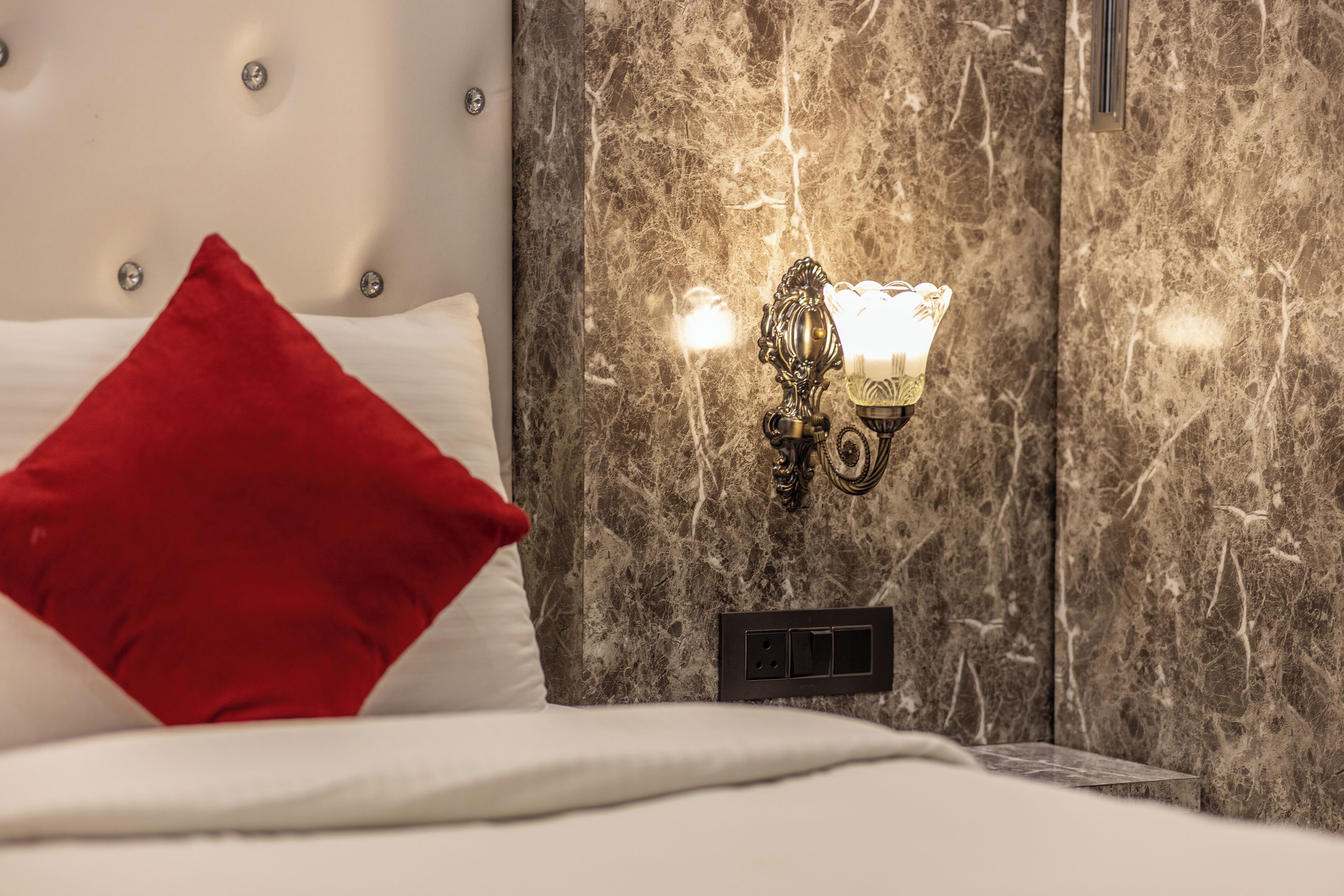 Un lit avec un oreiller rouge, un luminaire fixé au mur et un mur en marbre.