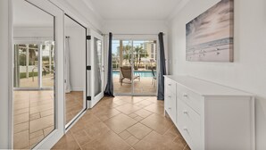 A hotel room with a sliding glass door leading to a pool area, a white dresser, and a painting on the wall.