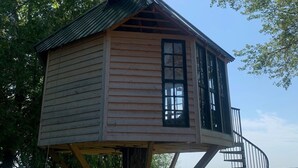 Una casa en árbol con escalera de metal, paredes de madera y vista al agua.