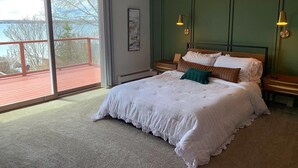Un dormitorio con un ventanal grande, una cama con ropa de cama blanca, dos mesitas de noche y una pared de acento verde.
