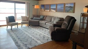 Una sala de estar con un sofá modular, un sillón pequeño, un tapete estampado y un ventanal con vistas al exterior.
