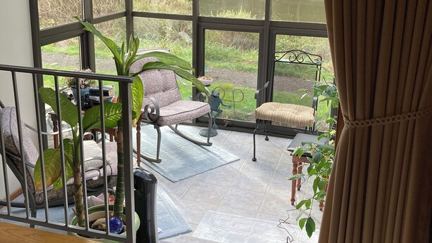 A conservatory with a glass roof, seating area, and a view of a pond. - Riverfront Beach House Rental (Yachats)