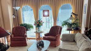 A living room with a sofa, two armchairs, a coffee table, and a rug. There are potted plants and a lamp on a side table. - Riverfront Beach House Rental (Yachats)