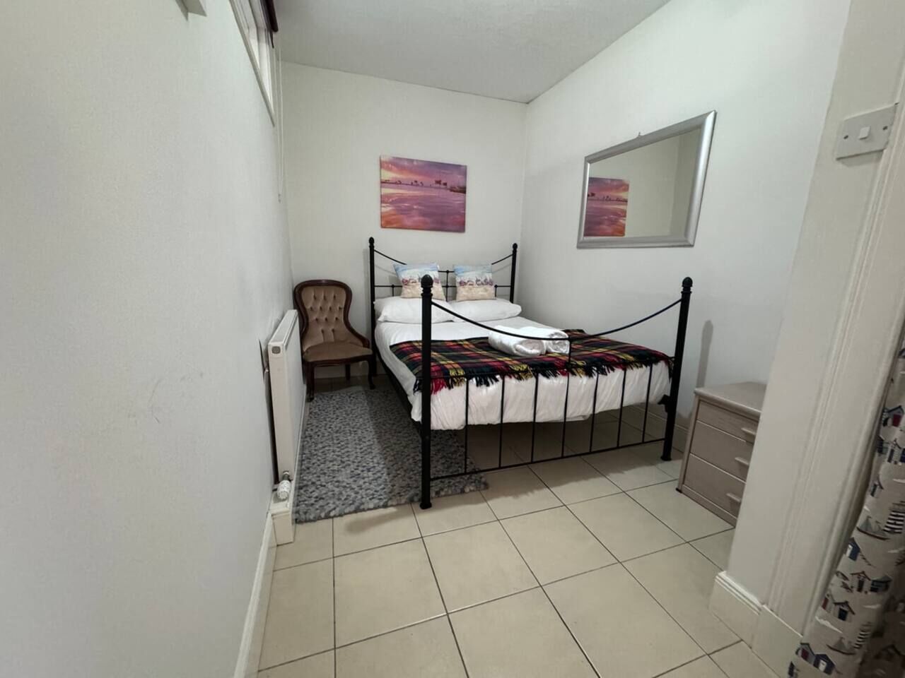 A small, narrow room with a single bed, a chair, a radiator, and a small cabinet.