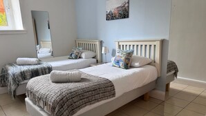 A bedroom with two single beds, a large mirror, and a painting on the wall. - The Fifie. A home away from home. (Saint Monans)