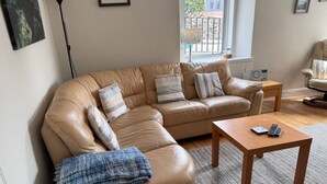 A living room with a tan leather sectional sofa, a wooden coffee table, and a small side table with a radio. - The Fifie. A home away from home. (Saint Monans)