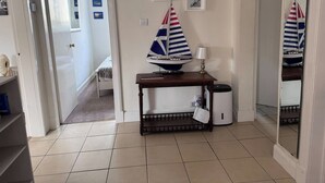 A room with a tiled floor, a wooden table with a model sailboat, a lamp, and a trash bin. - The Fifie. A home away from home. (Saint Monans)