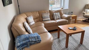 A living room with a tan leather sectional sofa, a wooden coffee table, and a small side table with a radio. - The Fifie. A home away from home. (Saint Monans)