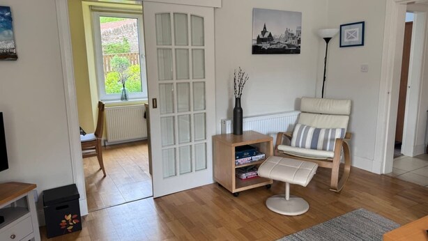 A living room with a wooden floor, a white sofa, a small wooden cabinet, and a radiator. - The Fifie. A home away from home. (Saint Monans)