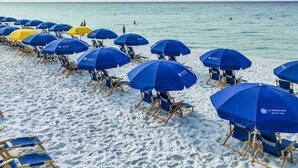 A beach with rows of blue and yellow umbrellas and wooden beach chairs.