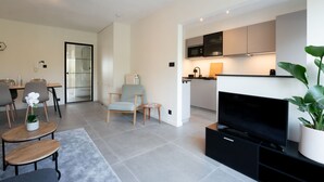 A modern living room with a flat-screen TV, a dining area with chairs and a table, and a kitchen with cabinets and a microwave. - 't Zout with balcony by Interhome (Bredene)