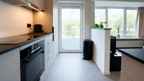 A modern kitchen with a built-in oven, a coffee machine, and a window with a view of greenery. - 't Zout with balcony by Interhome (Bredene)