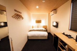 A compact hotel room with a bed, bedside table, TV, and a small desk area.