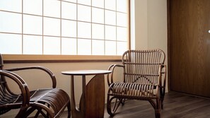 A room with a wooden floor, a large window with a grid pattern, and two wicker chairs with a small round table. - KonjakuSo Bentencho Rooftop Garden / Osaka Ōsaka (Osaka)
