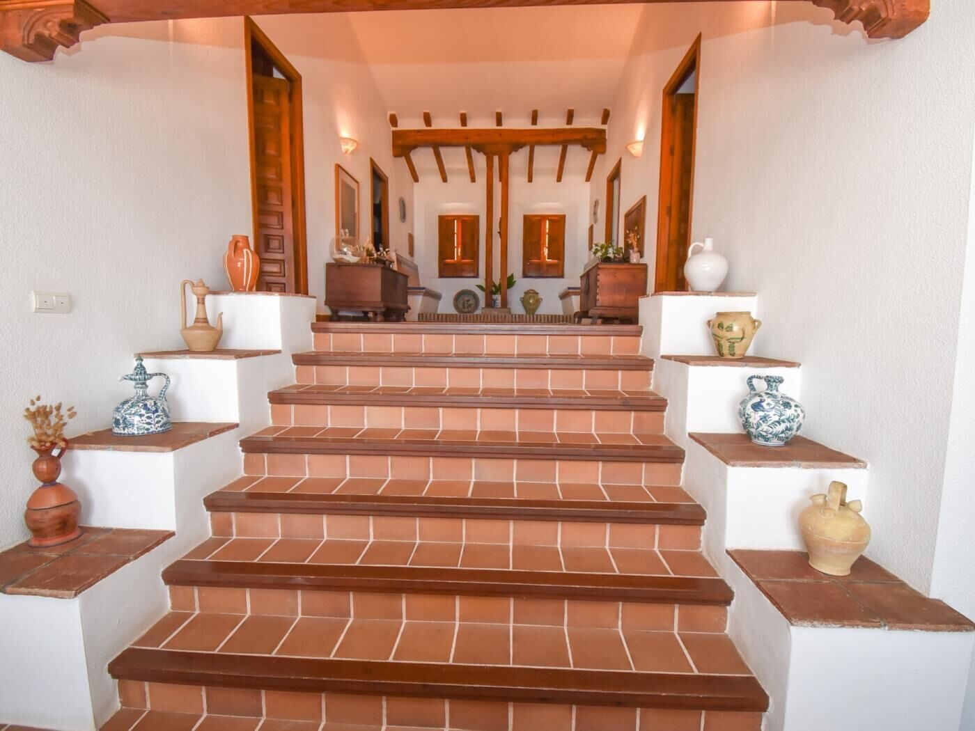 Una escalera de escalones de terracota que lleva a un rellano con techo de madera y un espejo.