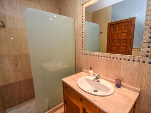 Een badkamer met een douchecabine van glas, een wastafel met spiegel erboven en een houten kast eronder.