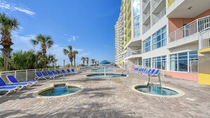 Área de piscina de hotel com várias piscinas, espreguiçadeiras e palmeiras.