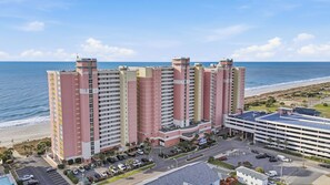 A multi-story hotel with a parking lot and a view of the beach.