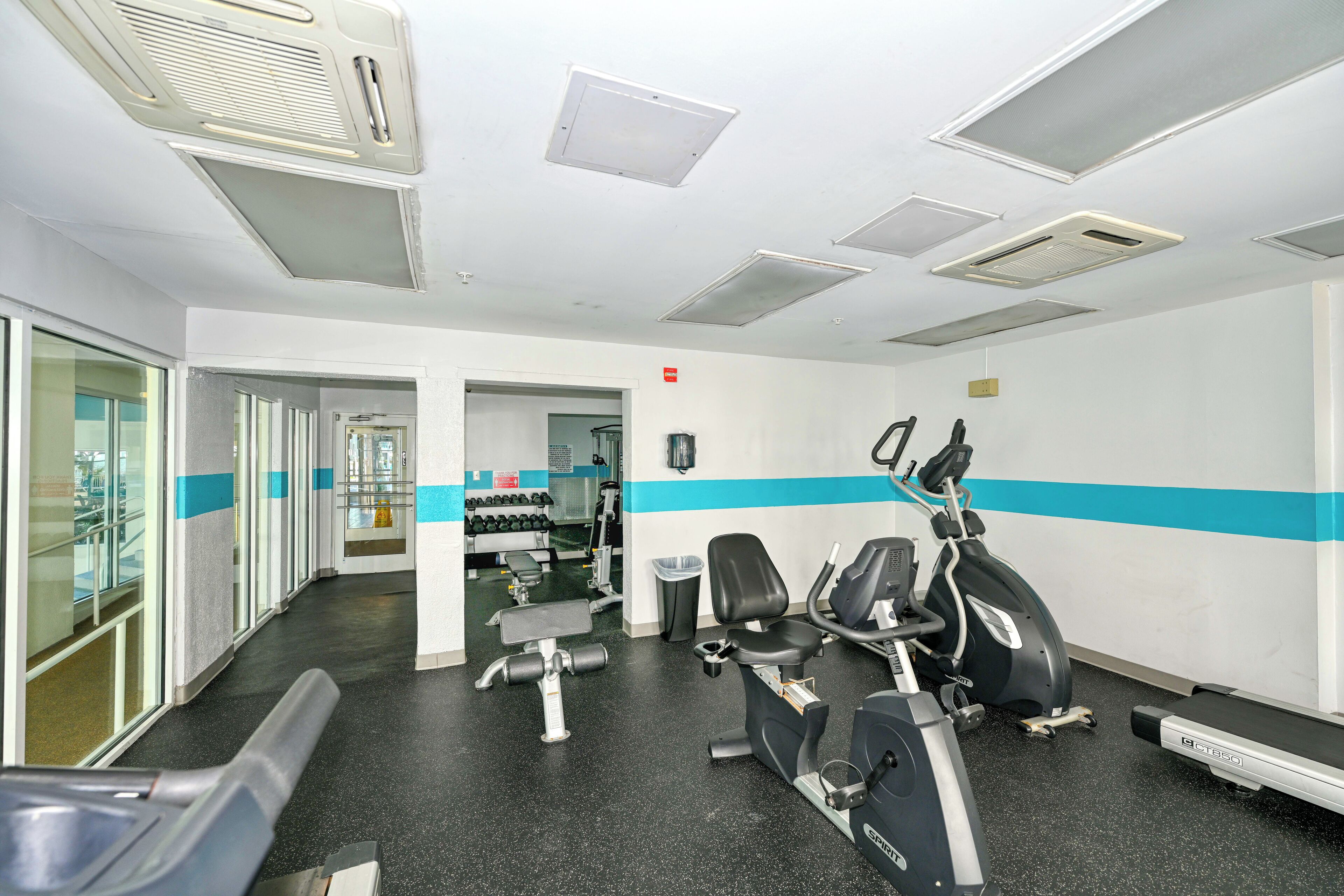 Une salle de sport équipée de matériel d’exercice, d’un banc et d’un mur orné d’une bande bleue.