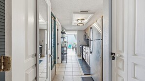 Um corredor estreito com uma área de cozinha à direita, com eletrodomésticos de aço inoxidável e piso em azulejos.
