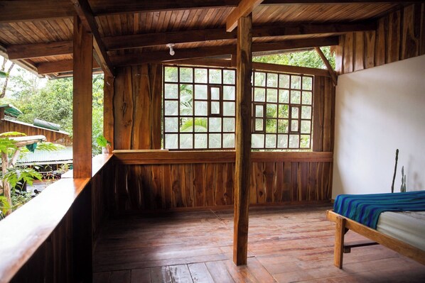 A wooden room with a large window, a bed, and a bench.
