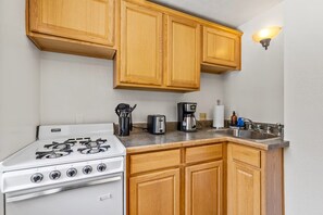A compact kitchen with a white stove, wooden cabinets, a toaster, a coffee maker, and a sink.