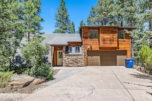 A two-story wooden house with a stone foundation, a garage, and a driveway leading to the entrance.