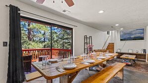 Uma sala de jantar com uma grande mesa de madeira posta para refeição, uma escada e um quadro na parede.