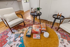 A living room with a patterned rug, two white chairs, a round coffee table, and a small side table with a plant.