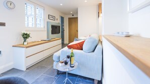 Eine moderne Küche mit Einbauofen und Mikrowelle, ein Essbereich mit Holztisch und Stühlen sowie eine gemütliche Sitzecke mit Sofa und kleinem Couchtisch.