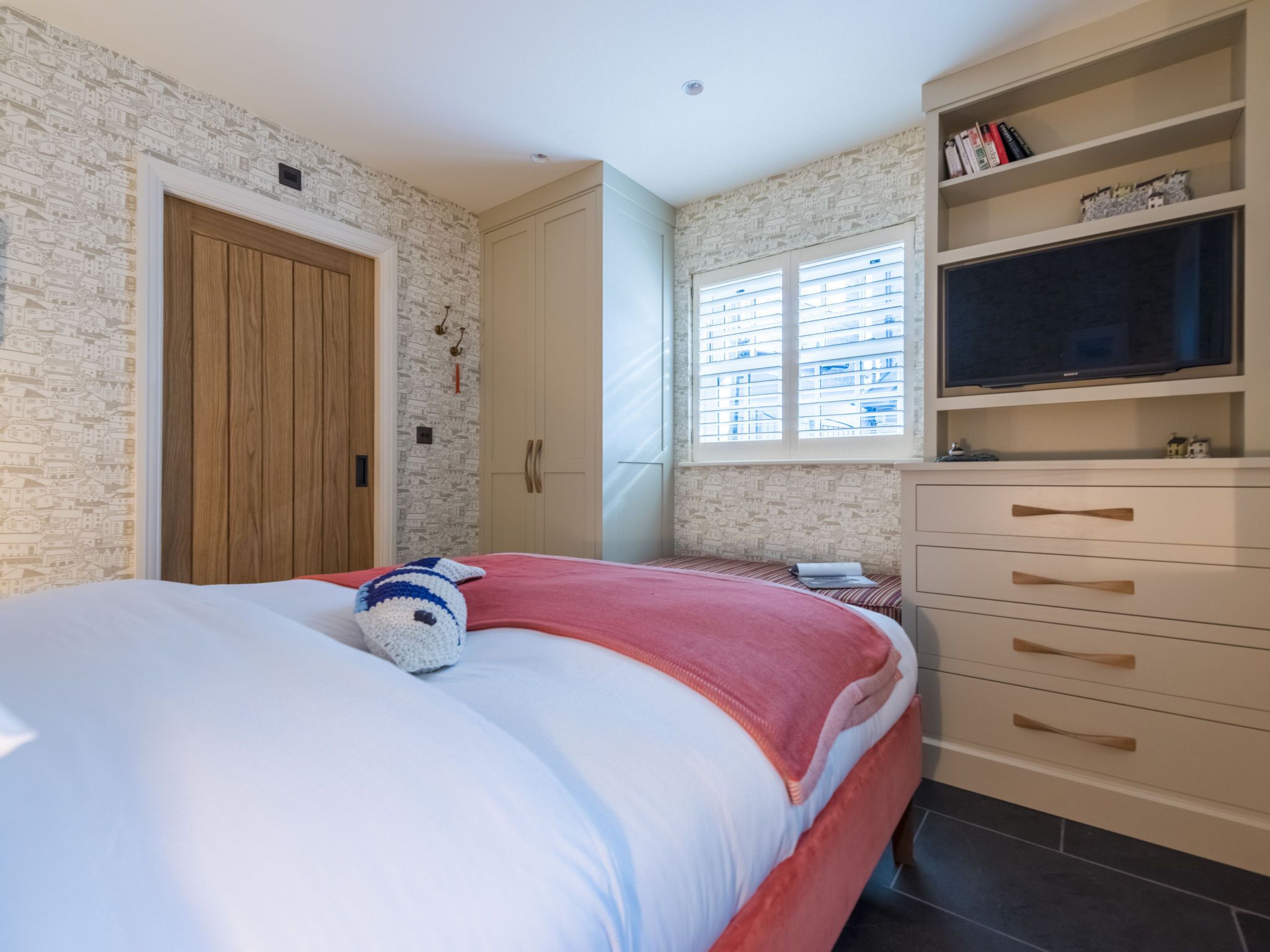 Une chambre à coucher comprenant un lit, une armoire, un téléviseur et une fenêtre avec des stores.