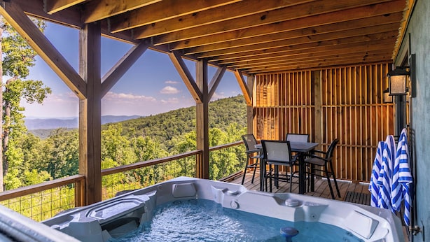 A wooden deck with a hot tub, outdoor seating, and a view of a forested mountain range. - Mountain Kandy - Luxury home with stunning views and amenities! (Boone)
