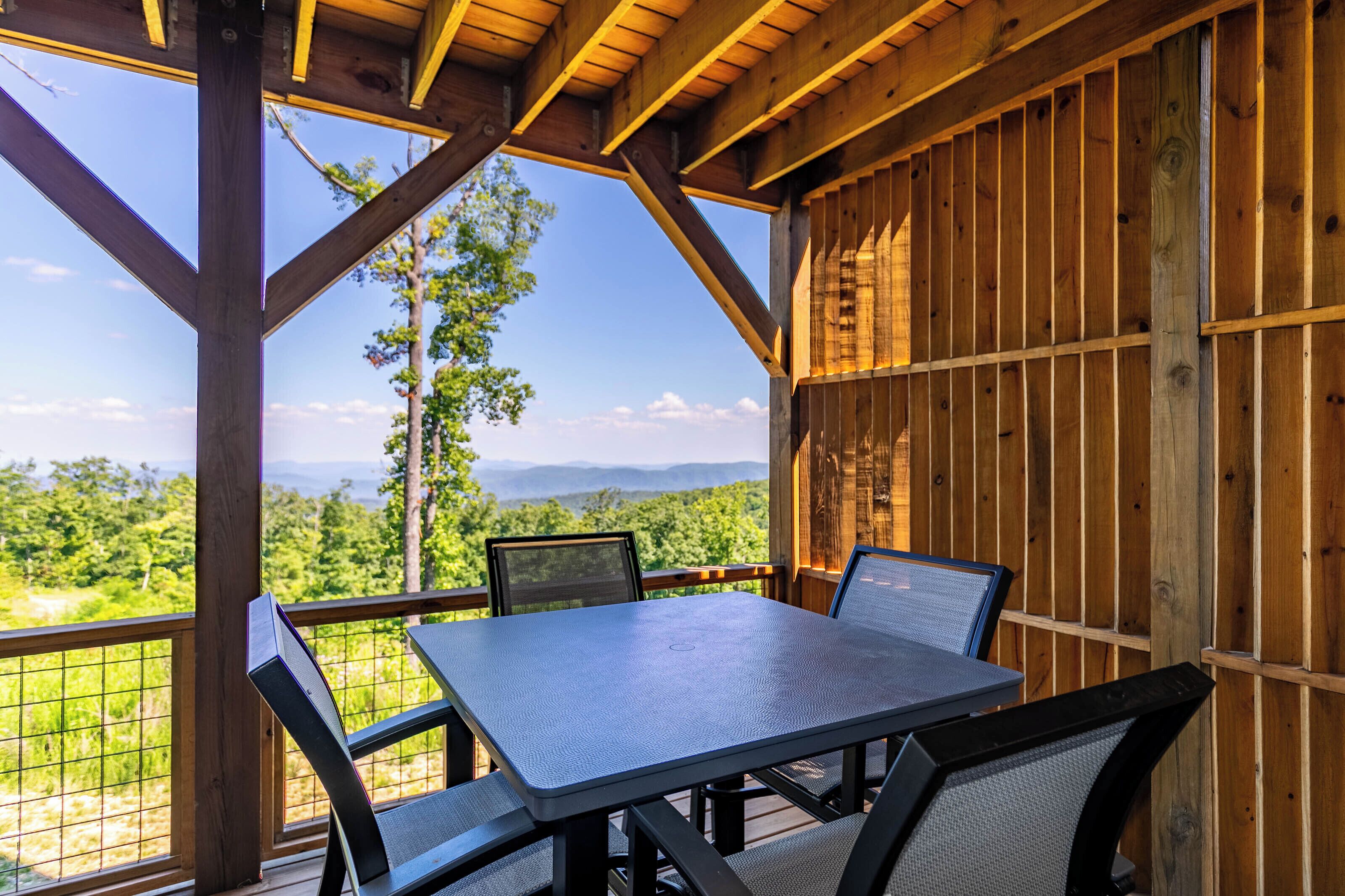 Une terrasse en bois avec une table et des chaises, offrant une vue sur un paysage montagneux.