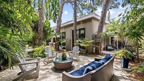 Une maison moderne dotée d’un patio aménagé avec des meubles en osier, un foyer et une végétation luxuriante.