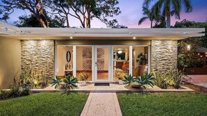 Une maison moderne avec une façade en pierre, une entrée dotée d’une porte en verre et une pelouse bien entretenue.