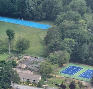 Vue aérienne d’un quartier résidentiel comprenant un court de tennis, un terrain de basketball et un espace jardin.