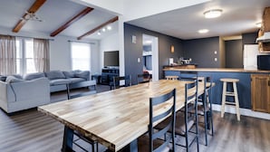 Una sala de estar moderna con una mesa de comedor de madera, un sofá gris y una cocina con armarios de madera y un taburete de bar.