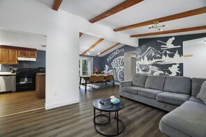 A modern living room with a grey sofa, a round coffee table, and a kitchen area with wooden cabinets and a built-in oven.