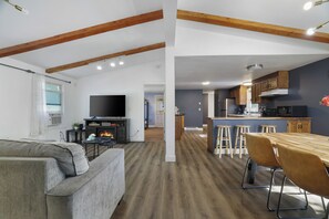 Una sala moderna con chimenea, un comedor con mesa de madera y taburetes de bar, y una cocina con armarios de madera y un microondas.