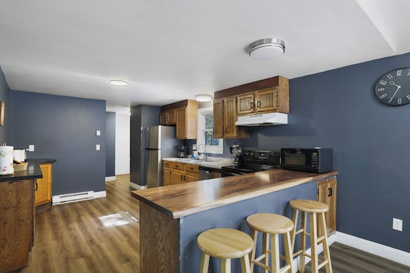 Una cocina moderna con armarios de madera, un refrigerador de acero inoxidable, un microondas y una zona de bar con taburetes.